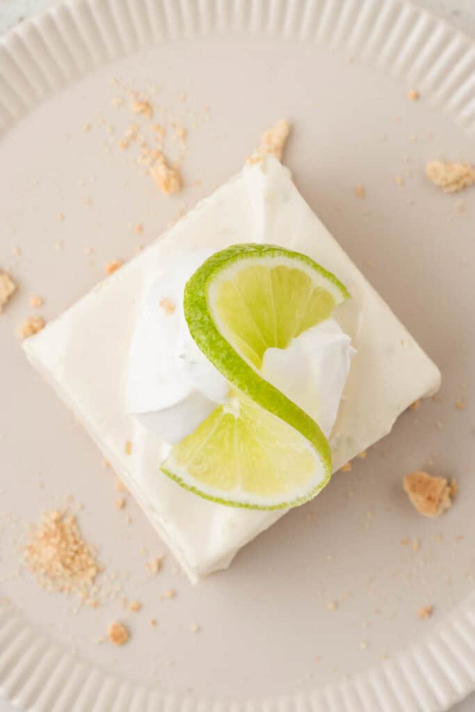 one key lime cheesecake bar on a plate topped with slice of lime
