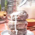 three applesauce fritters stacked on top of each other with vanilla glaze being spooned over the top