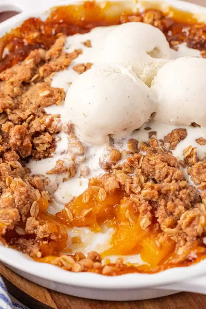 peach crisp with a scoop missing and ice cream melting over it