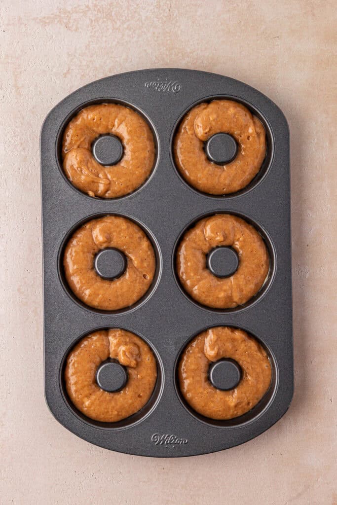 apple cider donut batter piped into a donut pan