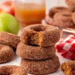 three apple cider donuts stacked on top of each other with the top donut having a bite taken out of it