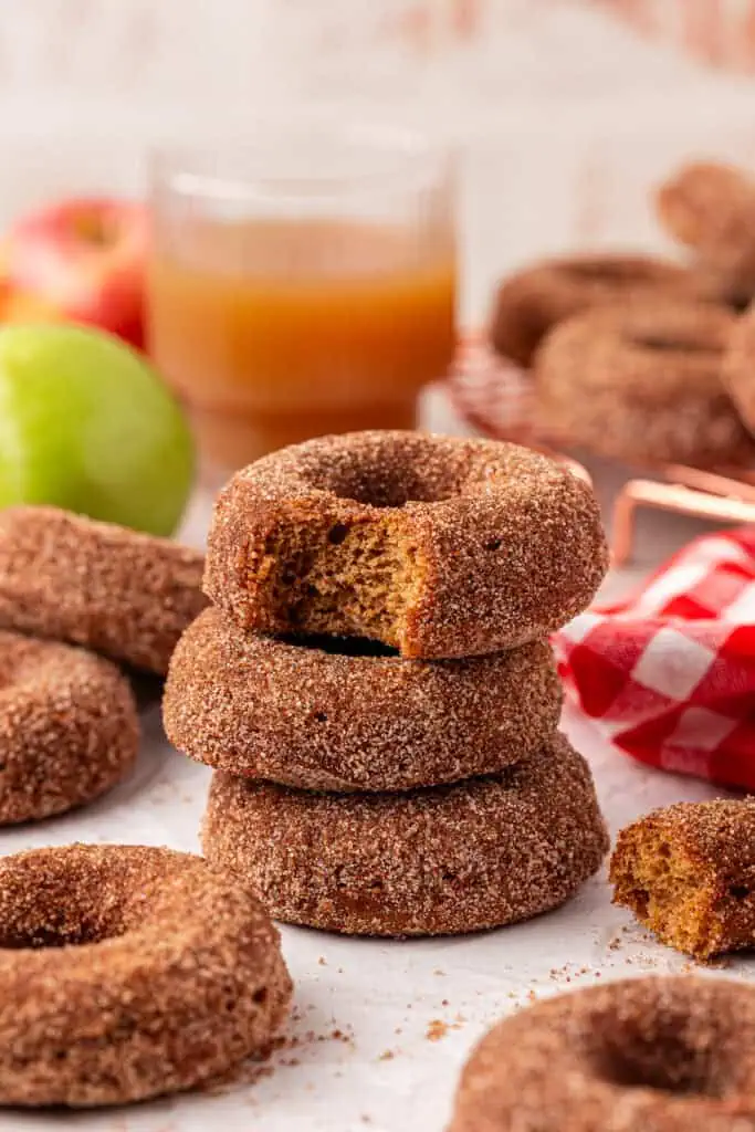 three apple cider donuts stacked on top of each other with the top donut having a bite taken out of it
