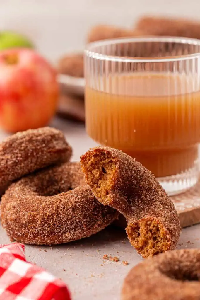 two apple cider donuts next to a cup of apple cider