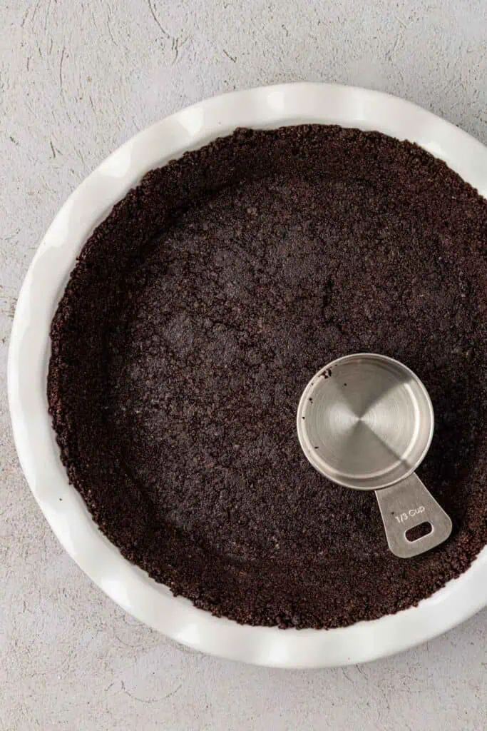 oreo cookie crust pressed down into a pie plate with the bottom of the measuring cup