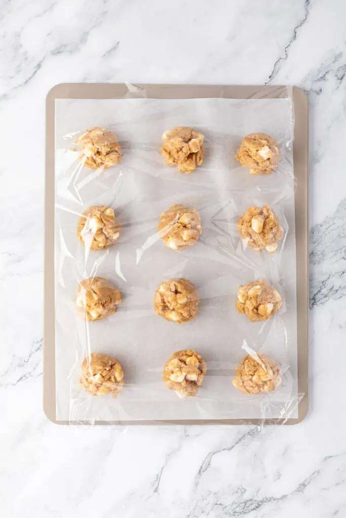 cookie dough balls scooped onto a cookie sheet and wrapped in plastic wrap