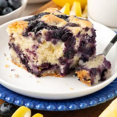 slice of blueberry cake with a forkful missing on a plate