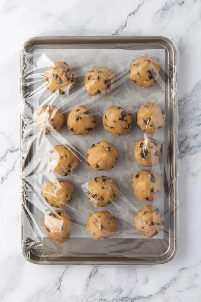 cookie dough balls wrapped in plastic wrap on a cookie sheet