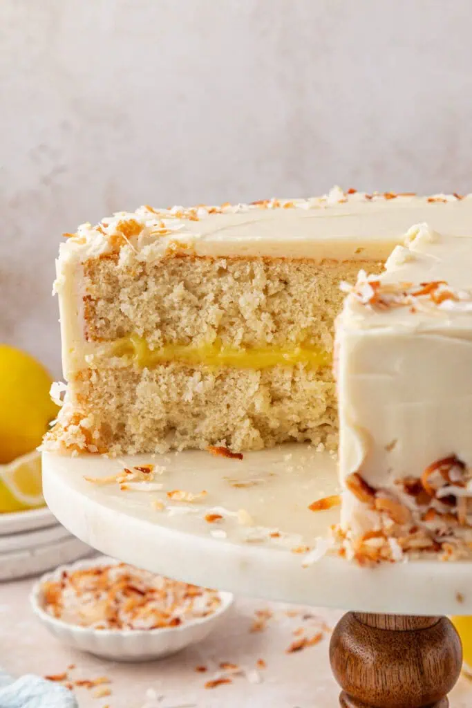 whole lemon coconut cake on a plate with a slice missing so you can see the inside