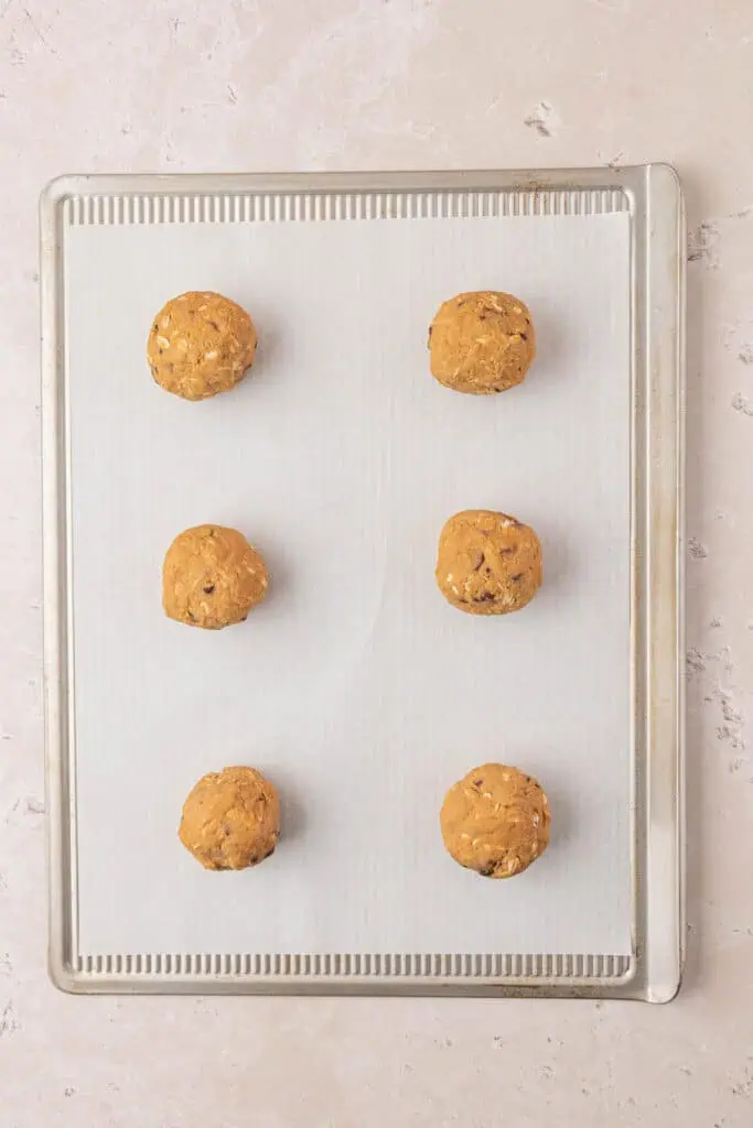 six cookie dough balls on a cookie sheet
