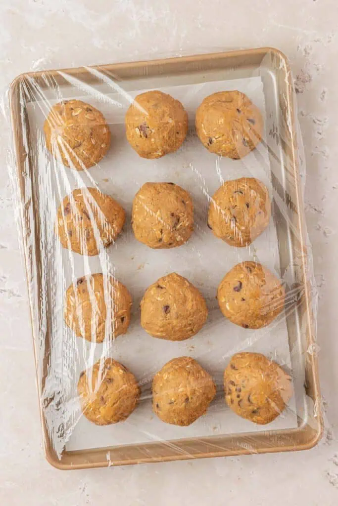 cookie dough balls on a cookie sheet wrapped in plastic wrap