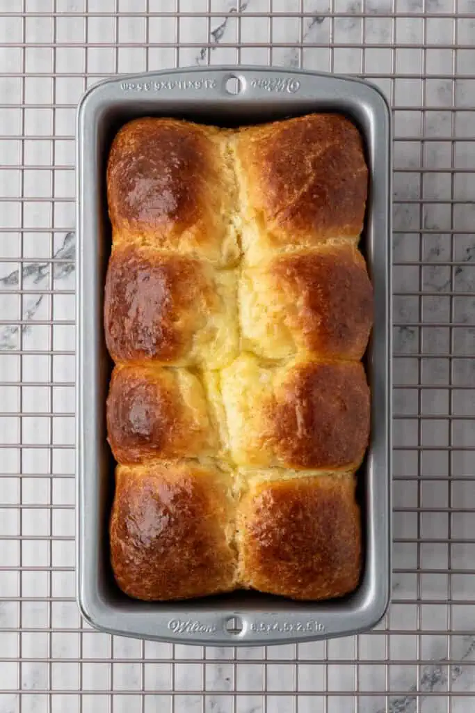 baked brioche in a loaf pan resting on a wire rack