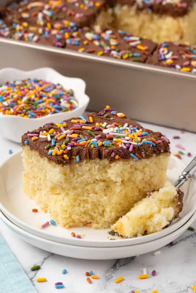 slice of yellow sheet cake with chocolate frosting on a plate with a fork