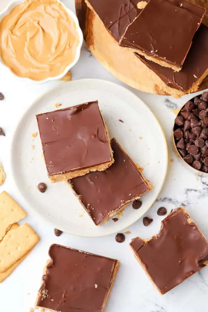 two bars on a plate surrounded by more bars and a bowl of peanut butter