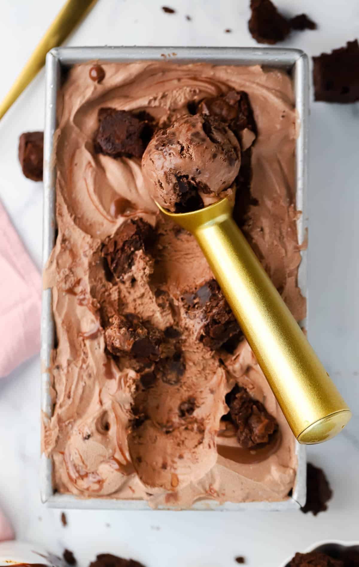 a loaf pan of brownie fudge ice cream with an ice cream scoop in it