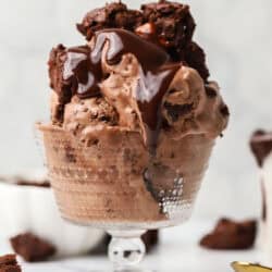 A glass dish of ice cream topped with hot fudge and chunks of brownie