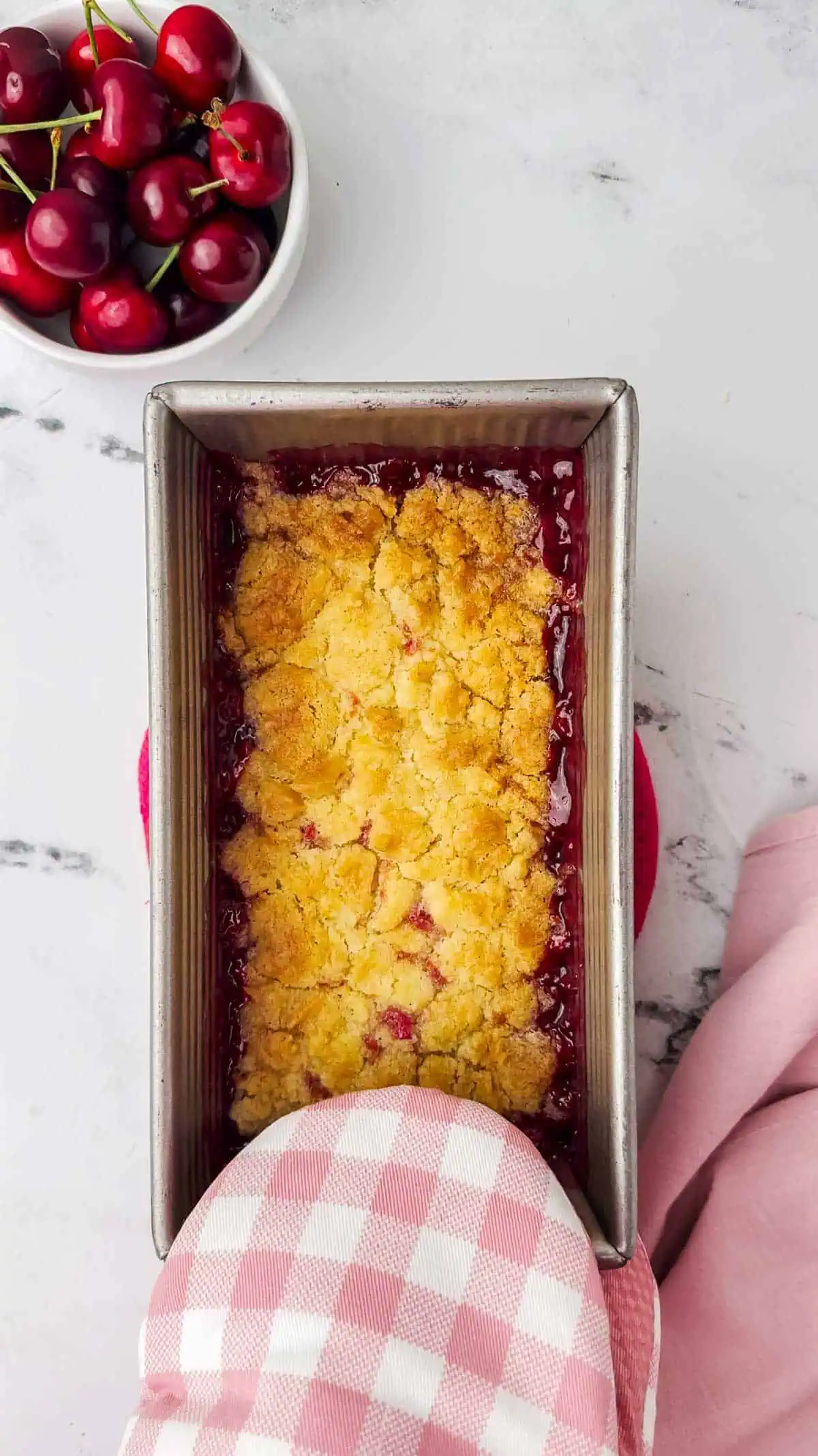 oven mitt holding a baked cherry cobbler