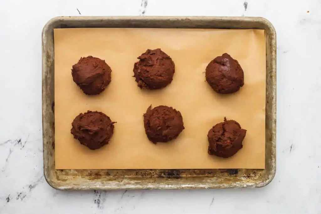 six cookie dough balls on a cookie sheet