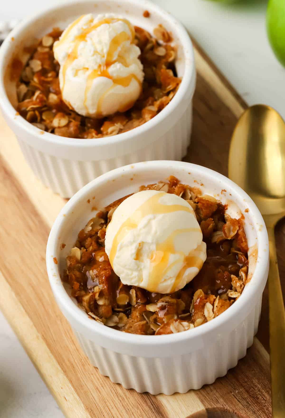 two ramekins of apple crisp topped with ice cream and caramel