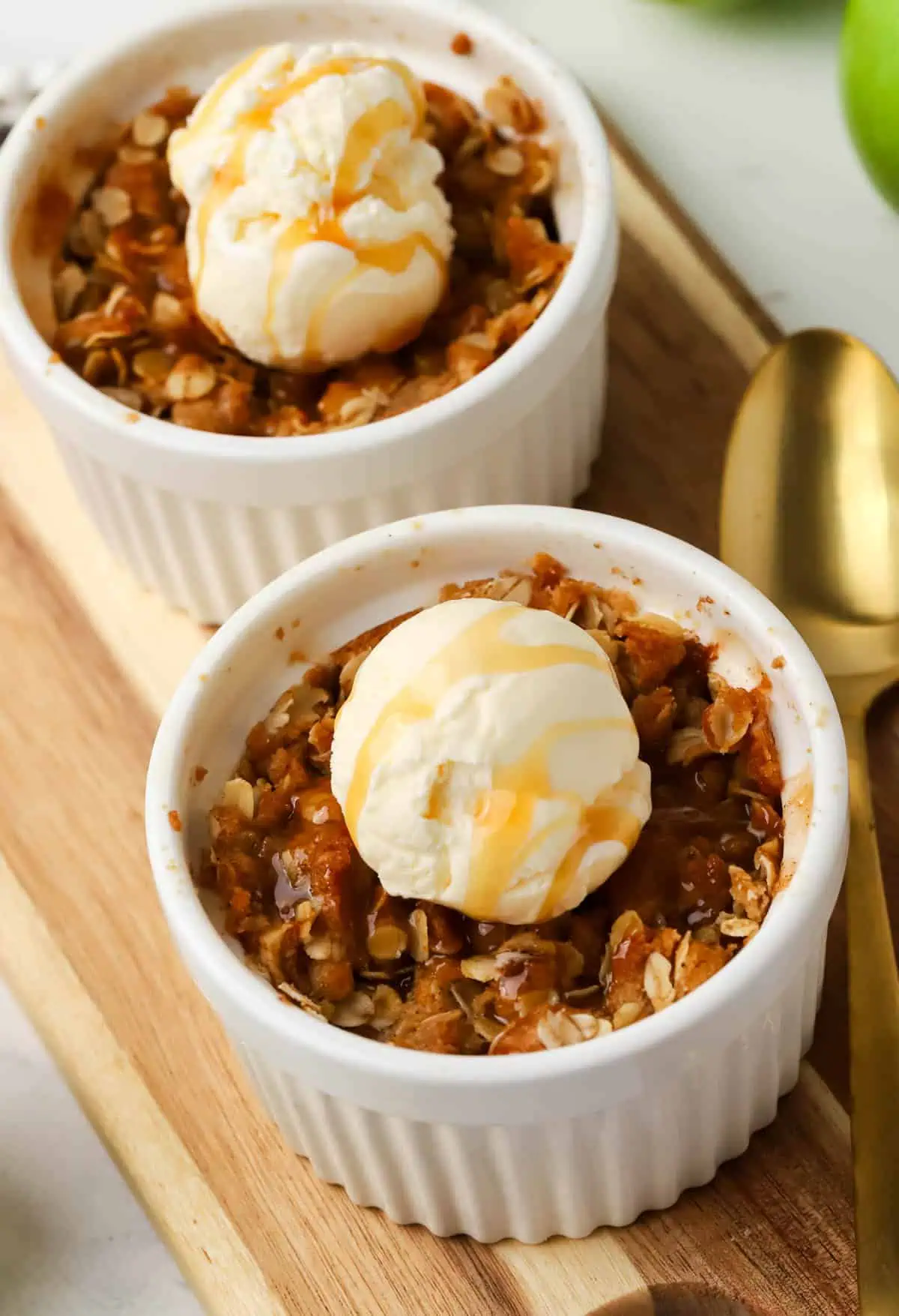 two ramekins of apple crisp topped with ice cream and caramel