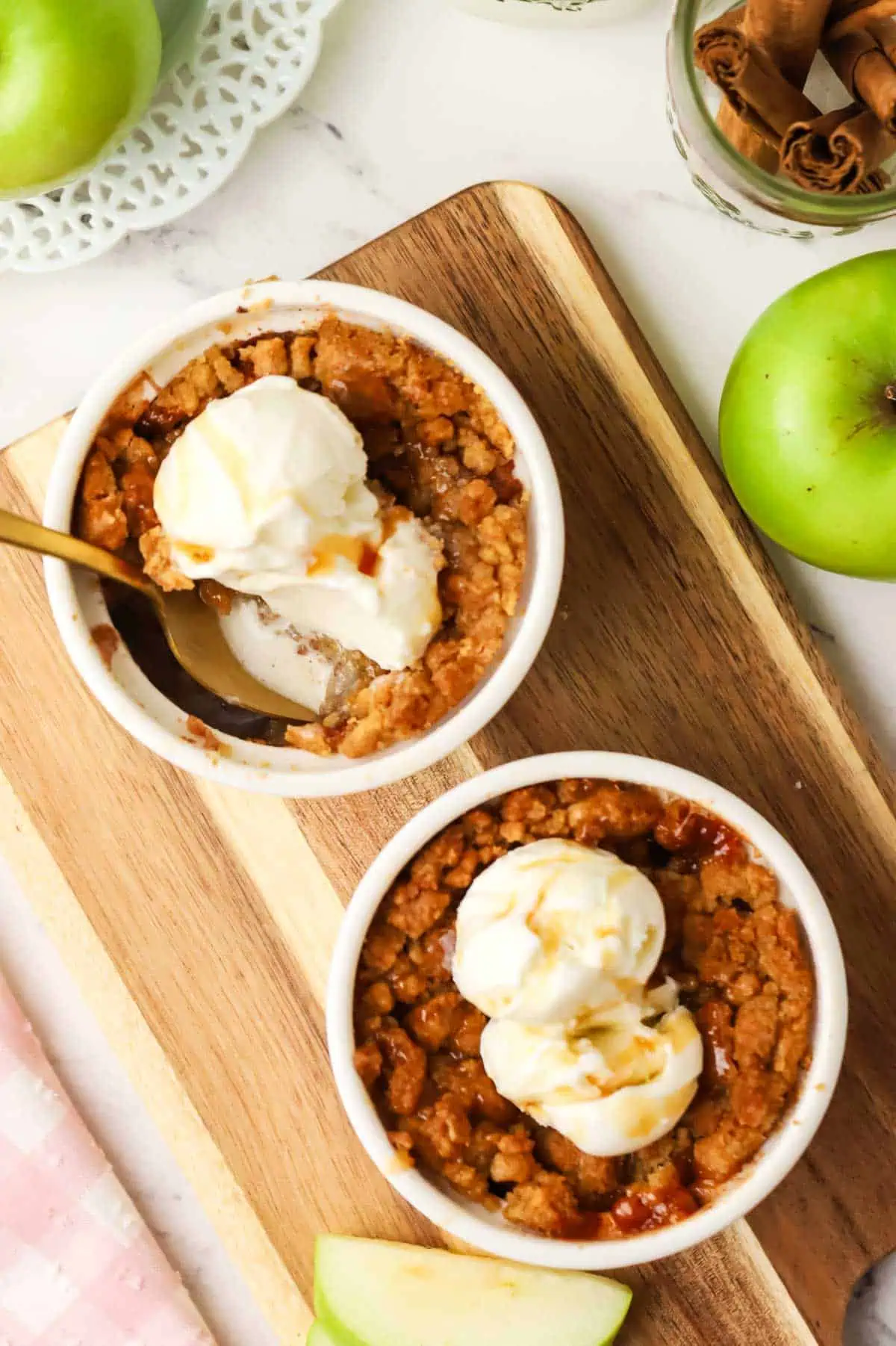 two apple crumbles topped with ice cream, caramel and a spoon in it