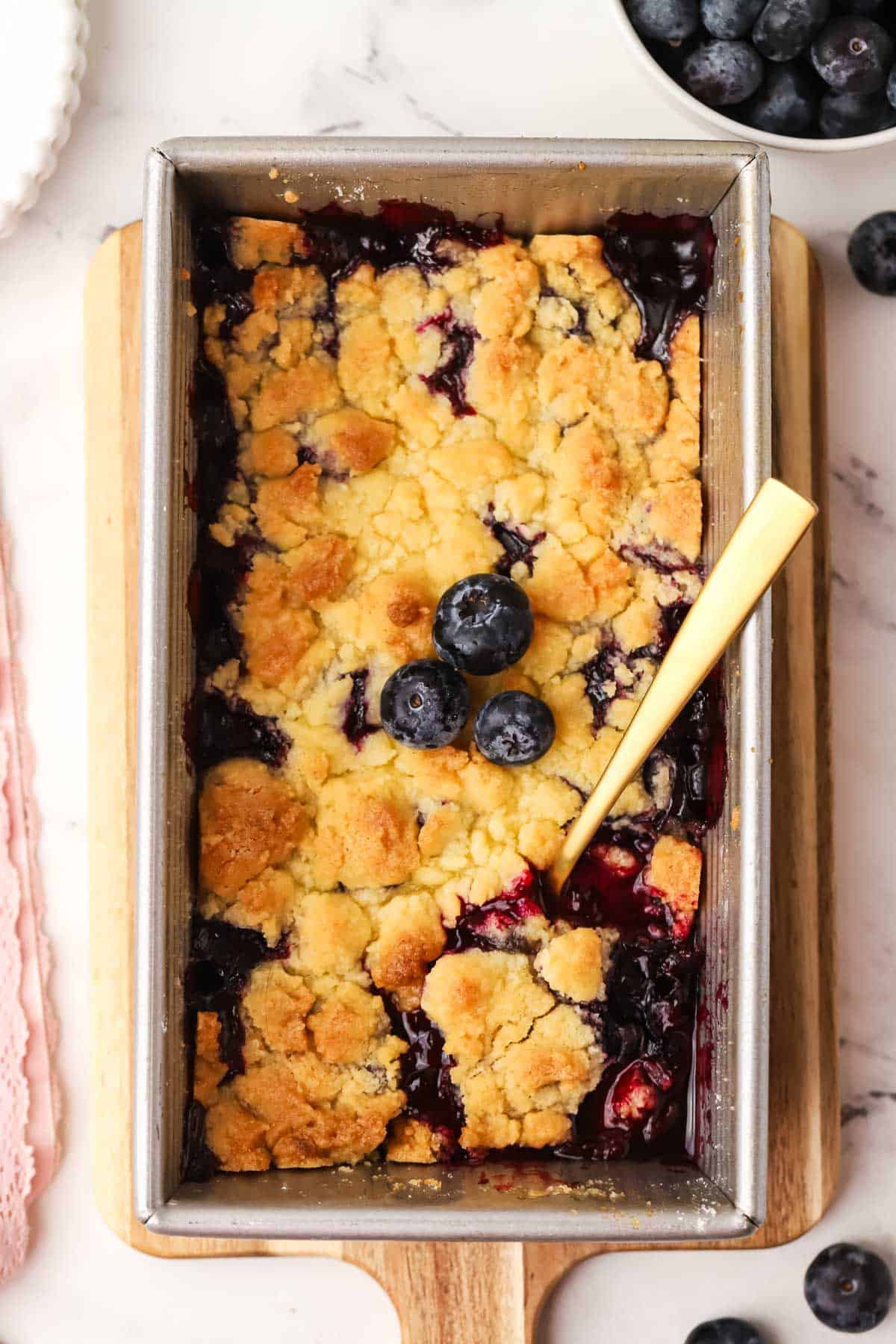 small batch blueberry crumble in a loaf pan with a spoon in it