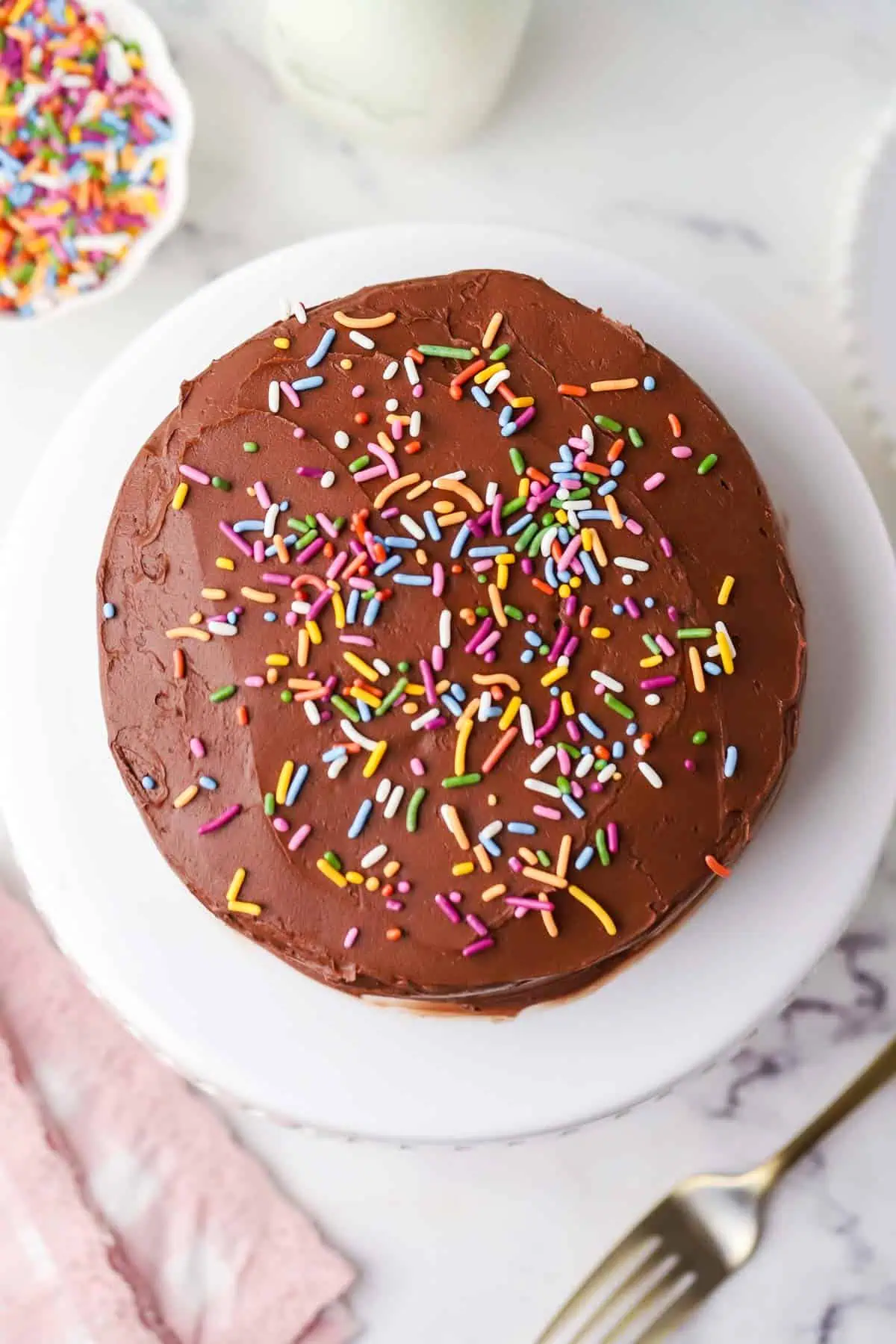 mini chocolate cake on a cake stand frosted and topped with sprinkles
