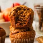 two pumpkin muffins stacked with the top muffin has a bite taken out of it