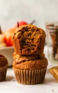 two pumpkin muffins stacked with the top muffin has a bite taken out of it